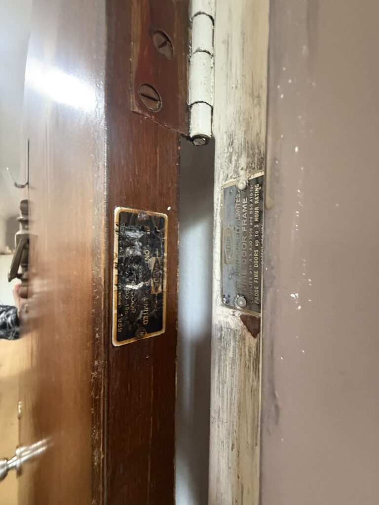 The leaf and frame tags on the hinge edge of an older fire door, the leaf tag dated 1969