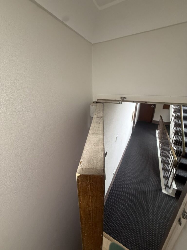The top edge of an older fire door, showing a layered grey core between the timber faces, below the door closer